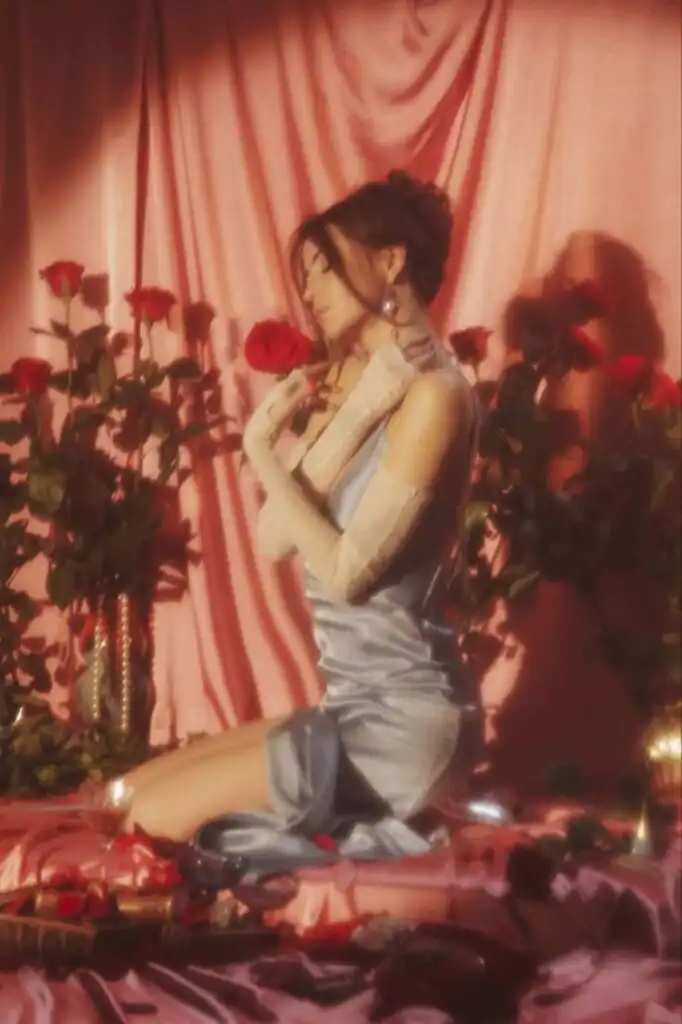 _ 1 Woman in elegant blue dress kneeling among roses, serene atmosphere with soft pink drapes and gentle lighting, evoking romantic elegance. | Sky Rye Design Woman in elegant blue dress kneeling among roses, serene atmosphere with soft pink drapes and gentle lighting, evoking romantic elegance.