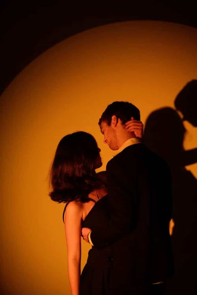 _ 10 Couple embracing in warm spotlight, casting shadows on the wall, creating a romantic atmosphere. | Sky Rye Design Couple embracing in warm spotlight, casting shadows on the wall, creating a romantic atmosphere.