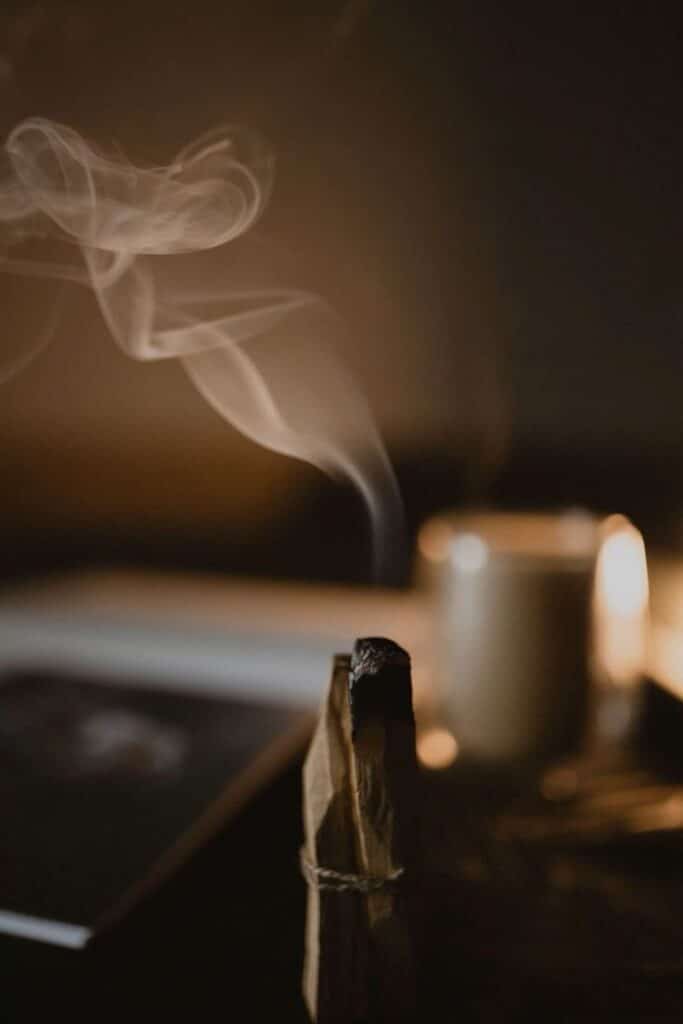 Burning Palo Santo stick releasing aromatic smoke, creating a calming ambiance in a dimly lit room with a blurred background.
