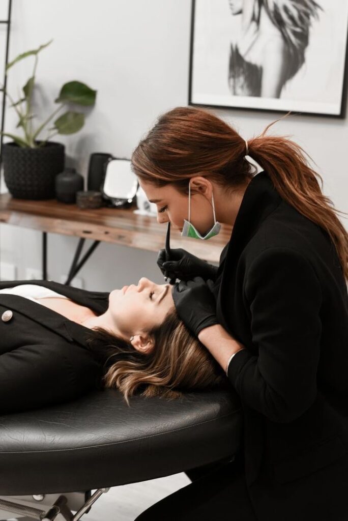 _ 13 Beautician in black gloves performing eyebrow microblading on a client in a salon, enhancing her look with precise strokes. | Sky Rye Design Beautician in black gloves performing eyebrow microblading on a client in a salon, enhancing her look with precise strokes.
