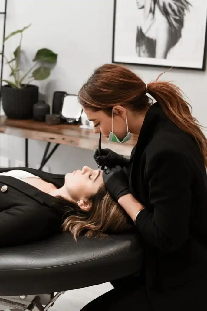 _ 13 Beautician in black gloves performing eyebrow microblading on a client in a salon, enhancing her look with precise strokes. | Sky Rye Design Beautician in black gloves performing eyebrow microblading on a client in a salon, enhancing her look with precise strokes.