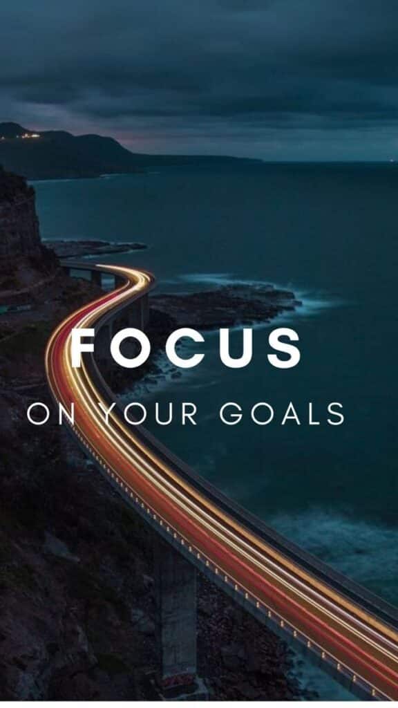 Scenic curving road by the ocean at night with Focus on Your Goals text overlay, inspiring perseverance and ambition.