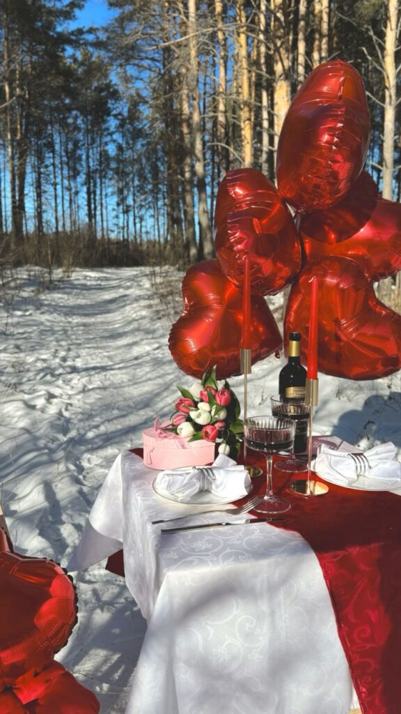 14 февраля идея фото Romantic winter picnic setup with red heart balloons, wine, and tulips on a snowy forest path, perfect for Valentine's Day. | Sky Rye Design Romantic winter picnic setup with red heart balloons, wine, and tulips on a snowy forest path, perfect for Valentine's Day.