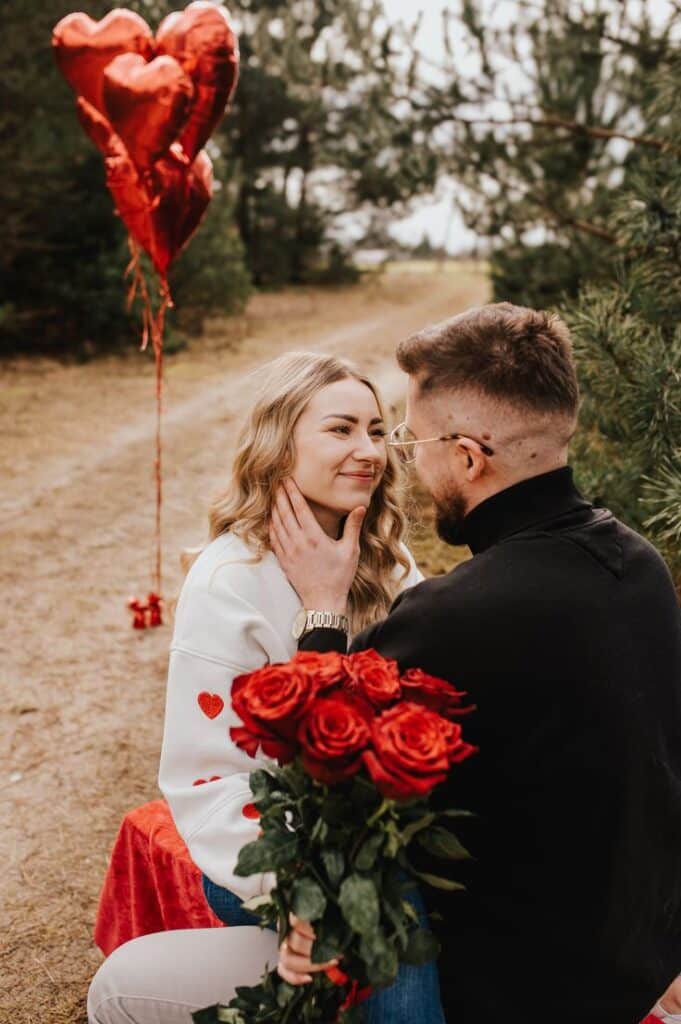 _ 15 Couple sharing a romantic moment in a forest with red roses and heart-shaped balloons, expressing love and affection. | Sky Rye Design Couple sharing a romantic moment in a forest with red roses and heart-shaped balloons, expressing love and affection. Valentine's Day Photography