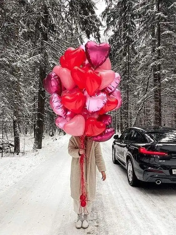 _ 16 Person holding red and pink heart-shaped balloons on a snowy forest road next to a black car. Winter love vibes. | Sky Rye Design Person holding red and pink heart-shaped balloons on a snowy forest road next to a black car. Winter love vibes.