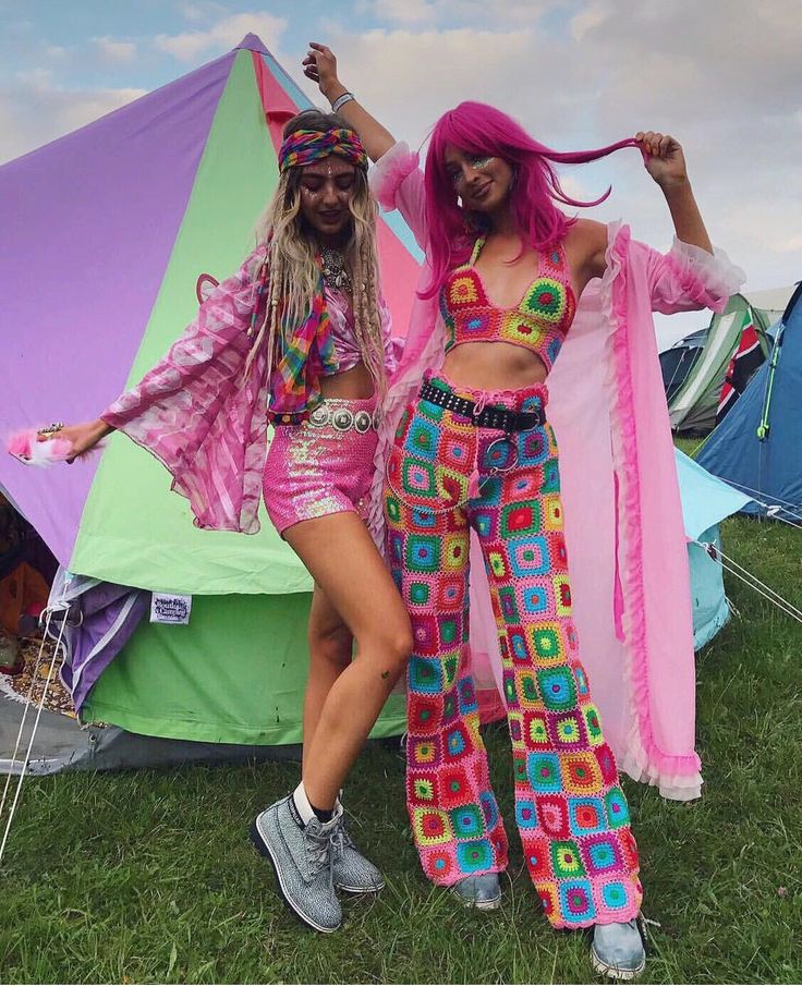 _ 17 Two people in vibrant festival outfits with pink elements pose by colorful tents on grass. | Sky Rye Design Two people in vibrant festival outfits with pink elements pose by colorful tents on grass.