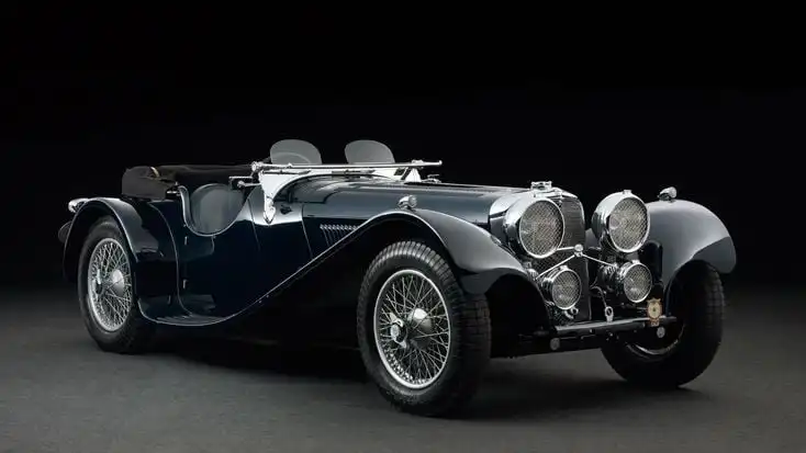 Vintage black convertible classic car with sleek design, chrome details, and wire wheels on a dark background.