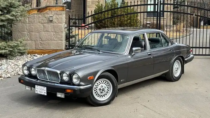Vintage luxury car parked in front of a wrought iron gate, featuring a classic design and sleek gray exterior.