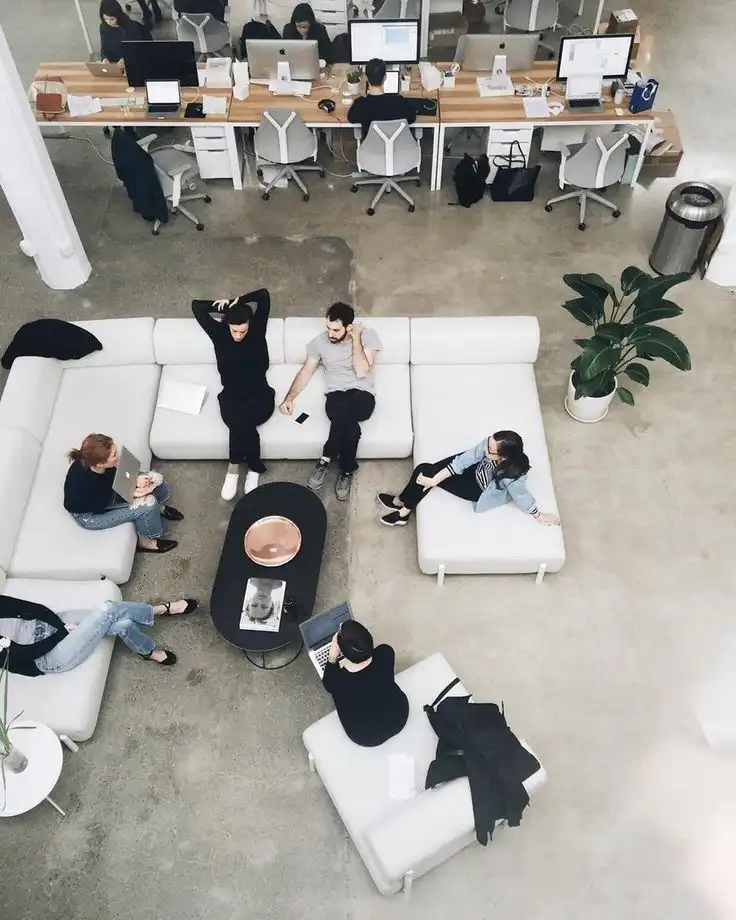 Overhead view of a modern open office space with people collaborating on white sofas and working at desks, fostering creativity and teamwork.