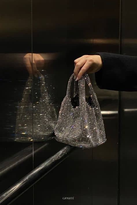 20 Off Iconic Crystal Bags Stylish hand holding a sparkling rhinestone handbag reflected in elevator mirrors, perfect for glamorous fashion accessories. | Sky Rye Design Stylish hand holding a sparkling rhinestone handbag reflected in elevator mirrors, perfect for glamorous fashion accessories.