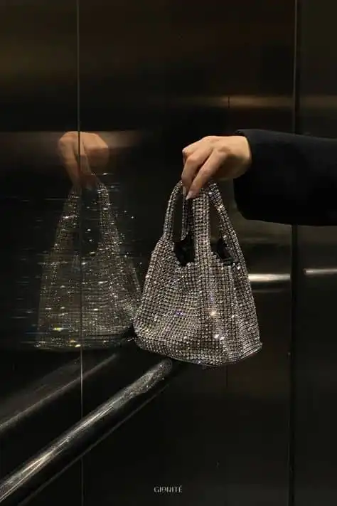 Stylish hand holding a sparkling rhinestone handbag reflected in elevator mirrors, perfect for glamorous fashion accessories.