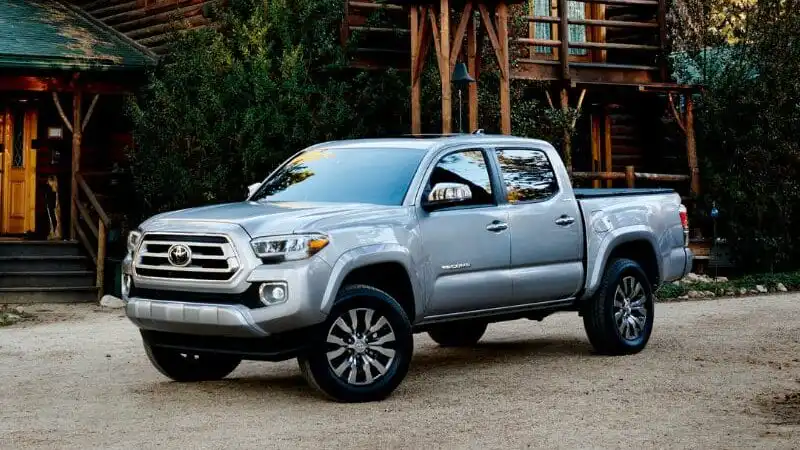 Silver pickup truck parked in front of a rustic log cabin surrounded by greenery and trees, showcasing outdoor adventure readiness.