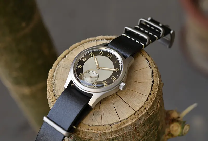 Vintage-style wristwatch with black leather strap and sleek dial, resting on a wooden log. Perfect for classic fashion enthusiasts.
