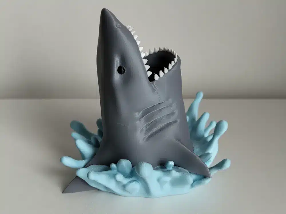 3D printed shark emerging from stylized water, showcasing detailed jaws and fins, ideal for marine-themed decor or toys.