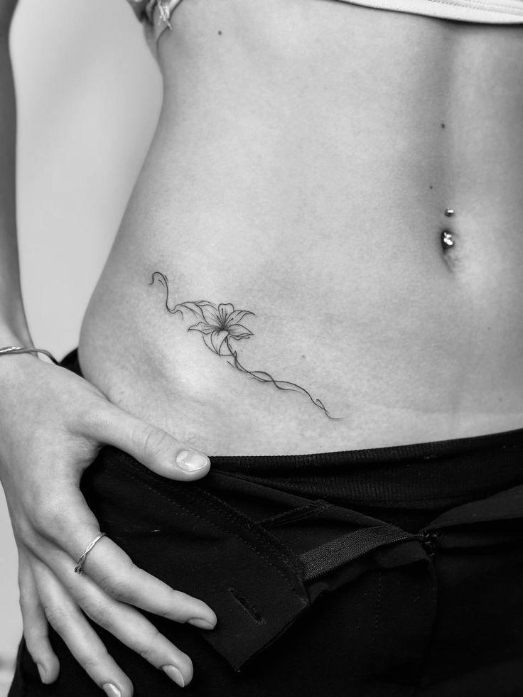 _ - 2026-01-04T190916986 Minimalist flower tattoo on lower abdomen, paired with navel piercing. Black and white close-up emphasizing body art details. | Sky Rye Design Minimalist flower tattoo on lower abdomen, paired with navel piercing. Black and white close-up emphasizing body art details.