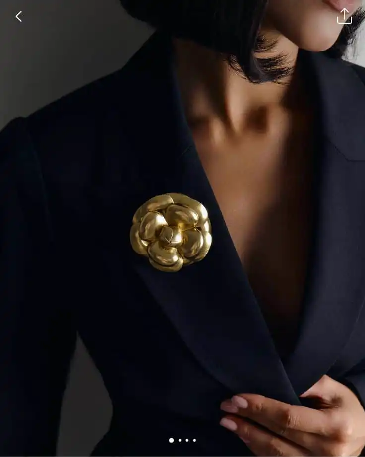 Woman in black blazer with elegant gold flower brooch, highlighting sophisticated fashion style and modern elegance.