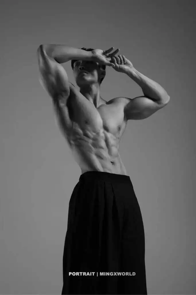 Athletic male posing shirtless, showcasing defined muscles in a dramatic black and white portrait.