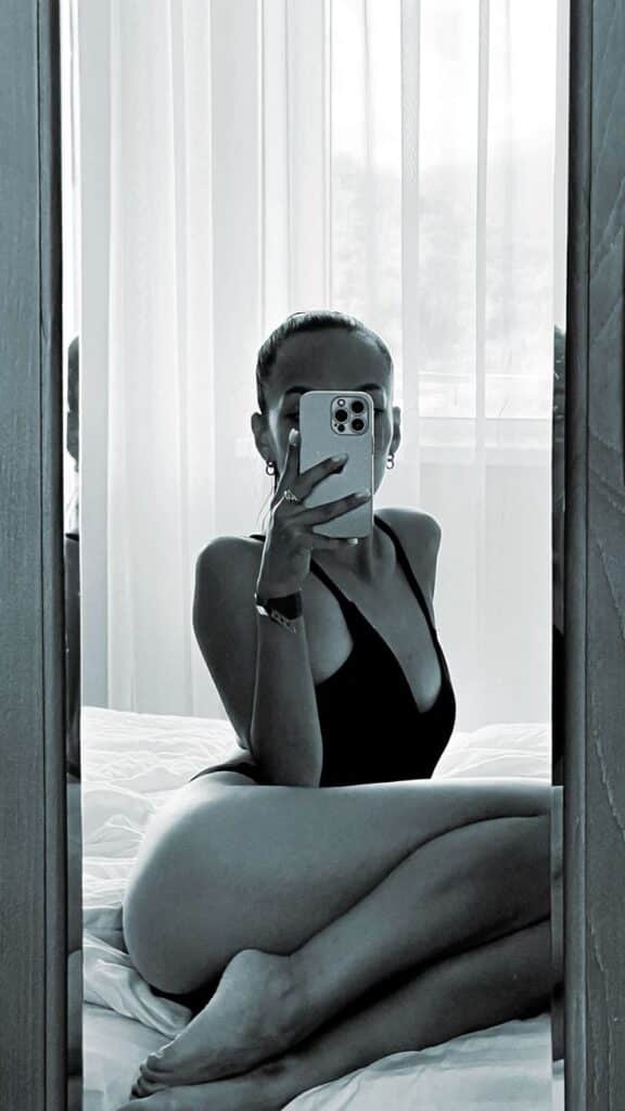 _ - 2026-01-10T225806564 Person in a black swimsuit takes a mirror selfie on a bed, framed by soft, sheer curtains in a minimalist room setting. | Sky Rye Design Person in a black swimsuit takes a mirror selfie on a bed, framed by soft, sheer curtains in a minimalist room setting.