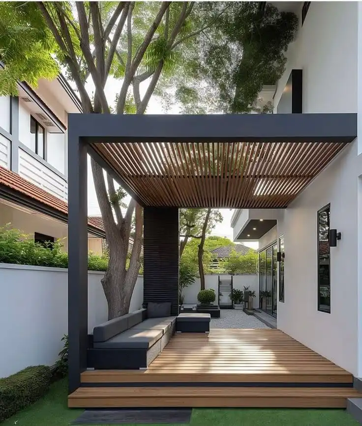 Screenshot Modern outdoor patio with wooden deck, minimalist furniture, and garden view under a sleek pergola attached to a contemporary house. | Sky Rye Design Modern outdoor patio with wooden deck, minimalist furniture, and garden view under a sleek pergola attached to a contemporary house.