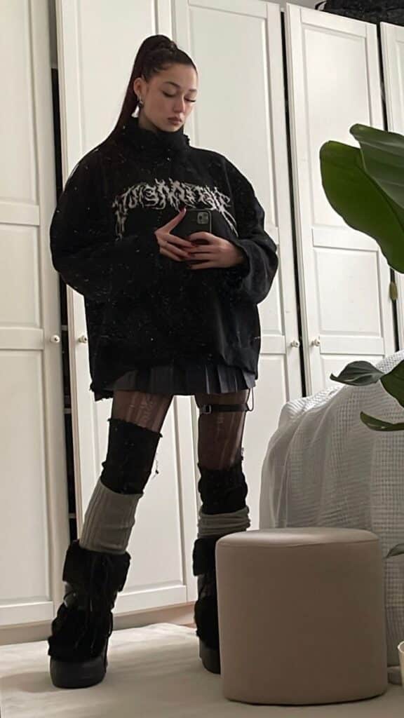 _ 22 Stylish woman in black oversized sweater, patterned tights, and platform boots, taking a mirror selfie in a modern bedroom. | Sky Rye Design Stylish woman in black oversized sweater, patterned tights, and platform boots, taking a mirror selfie in a modern bedroom.