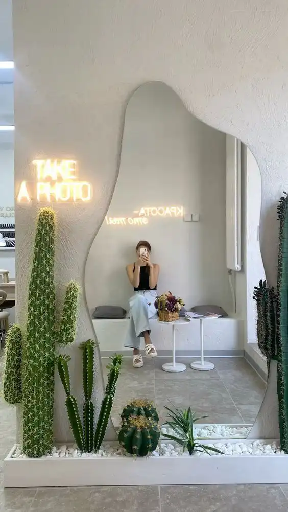 Modern interior with mirror reflection of sitting person, surrounded by cacti and neon sign, creating a stylish, contemporary scene.