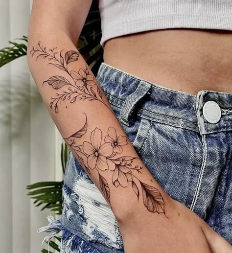 Arm with detailed floral tattoo art, wearing denim shorts and crop top, showcasing intricate design and casual summer style.