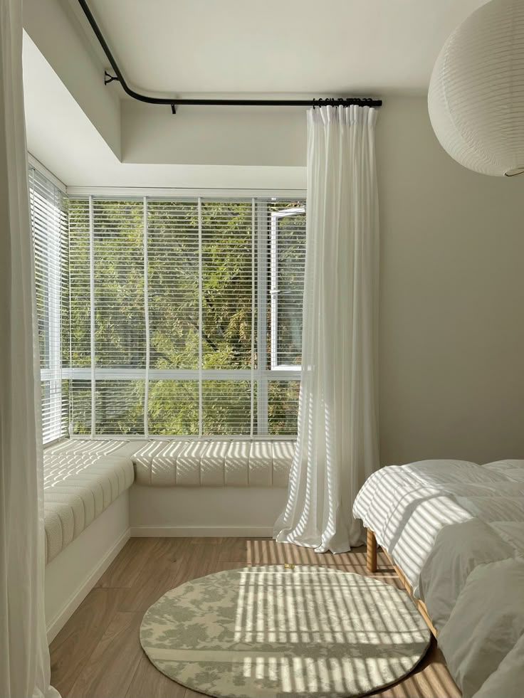 _ 25 Bright bedroom with large windows, sheer curtains, and a cozy window seat. Sunlight casts shadows on a round rug and wooden floor. | Sky Rye Design Bright bedroom with large windows, sheer curtains, and a cozy window seat. Sunlight casts shadows on a round rug and wooden floor.