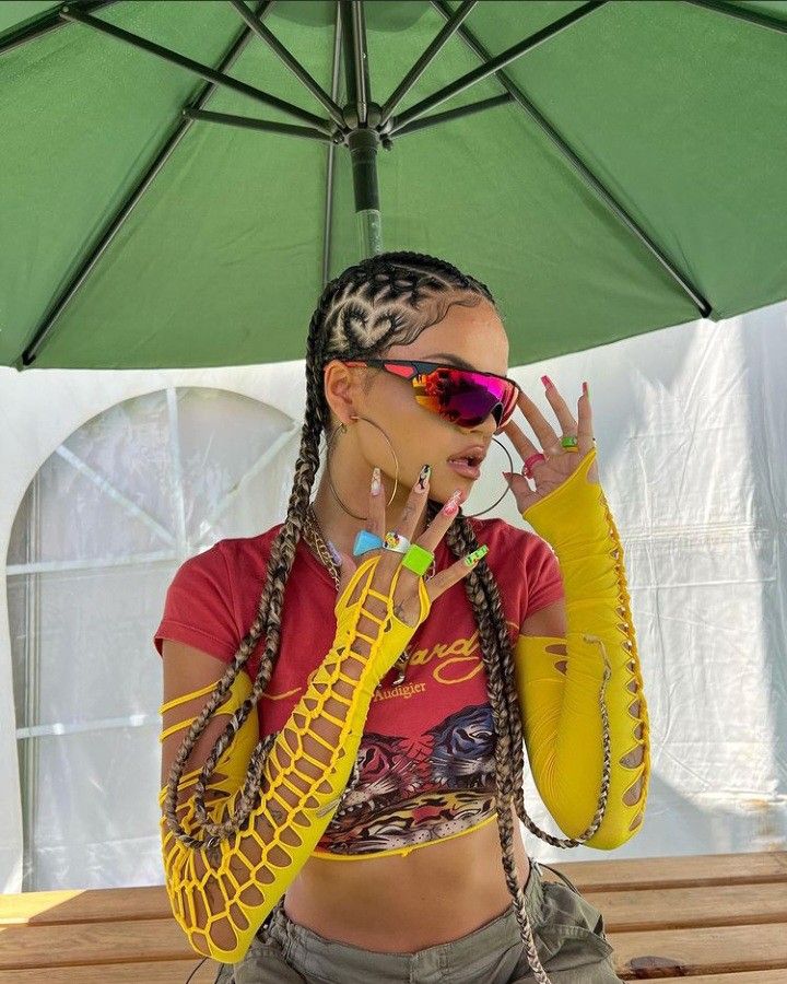 _ 25 Fashionable woman in colorful outfit and braids poses under green umbrella, wearing sporty sunglasses and yellow mesh | Sky Rye Design Fashionable woman in colorful outfit and braids poses under green umbrella, wearing sporty sunglasses and yellow mesh