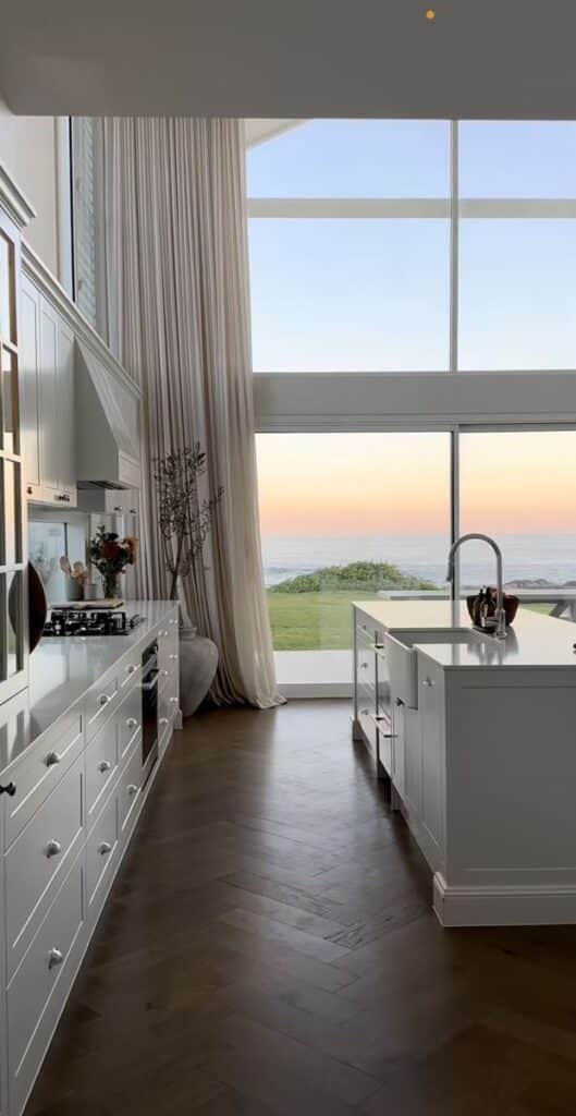 _ 26 Modern kitchen with large windows, white cabinets, and ocean view at sunset, creating a serene and elegant cooking space. | Sky Rye Design Modern kitchen with large windows, white cabinets, and ocean view at sunset, creating a serene and elegant cooking space.
