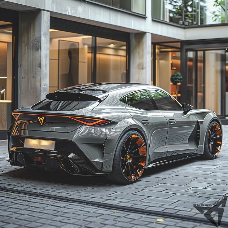261297ca-e582-47c3-9fb8-805589079db7 Sleek gray sports car with black and orange rims parked outside a modern building. | Sky Rye Design Sleek gray sports car with black and orange rims parked outside a modern building.