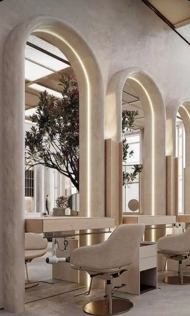 Stylish modern salon interior with elegant arch mirrors, beige chairs, and underlit decor creating a chic, luxurious atmosphere.
