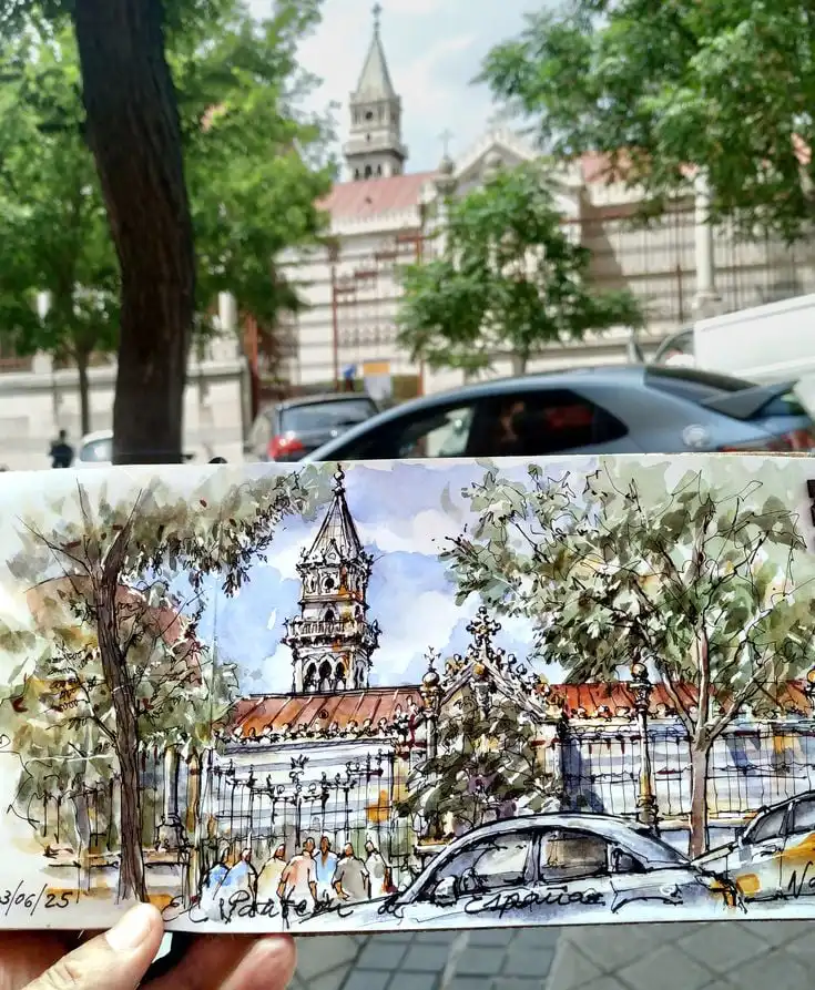 Hand-drawn sketch of a historic church held up in front of the actual building, surrounded by trees and parked cars on a sunny day.