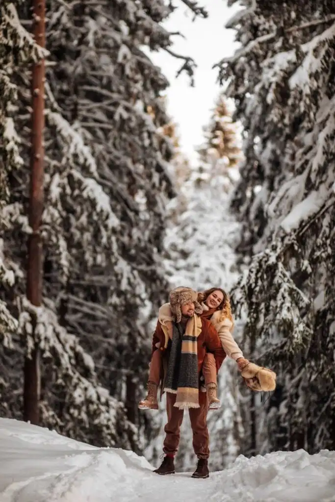 _ 3 Couple enjoying a playful winter moment in a snowy forest, surrounded by frosted trees, bundled in cozy outfits and scarves. | Sky Rye Design Couple enjoying a playful winter moment in a snowy forest, surrounded by frosted trees, bundled in cozy outfits and scarves.