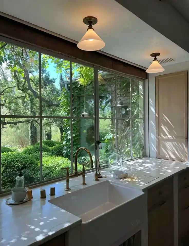 _ 33 Bright kitchen with large windows overlooking a lush garden, featuring a farmhouse sink, brass faucet, and elegant pendant lights. | Sky Rye Design Bright kitchen with large windows overlooking a lush garden, featuring a farmhouse sink, brass faucet, and elegant pendant lights.