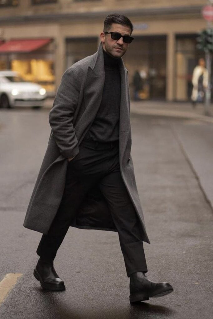 Man in stylish gray coat and sunglasses walking on city street, showcasing trendy winter fashion with confidence.