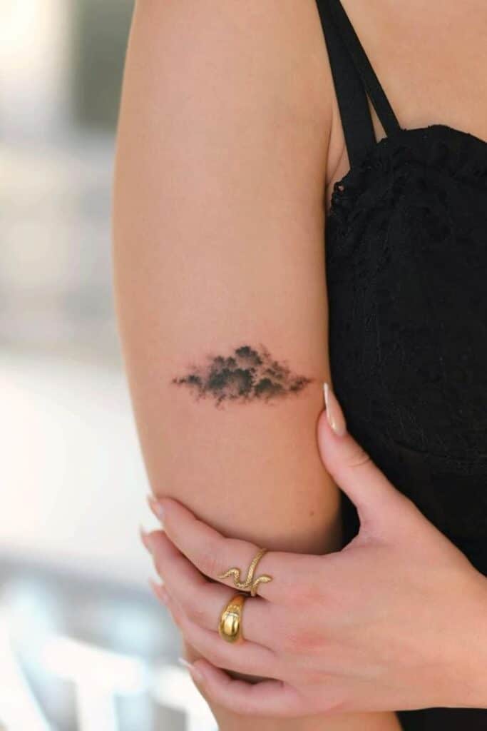 37 Best Cool Small Tattoo Ideas Elegant cloud tattoo on woman's arm, complemented by black dress and gold rings, showcasing minimalist body art and stylish fashion. | Sky Rye Design Elegant cloud tattoo on woman's arm, complemented by black dress and gold rings, showcasing minimalist body art and stylish fashion.
