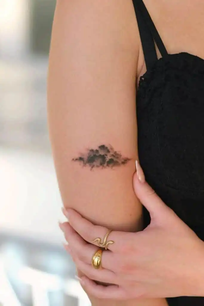 37 Best Cool Small Tattoo Ideas Elegant cloud tattoo on woman's arm, complemented by black dress and gold rings, showcasing minimalist body art and stylish fashion. | Sky Rye Design Elegant cloud tattoo on woman's arm, complemented by black dress and gold rings, showcasing minimalist body art and stylish fashion.