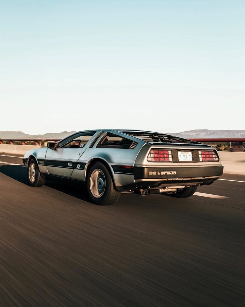 Iconic silver DeLorean sports car cruising on a highway under a clear blue sky, capturing the essence of 1980s retro automotive design.