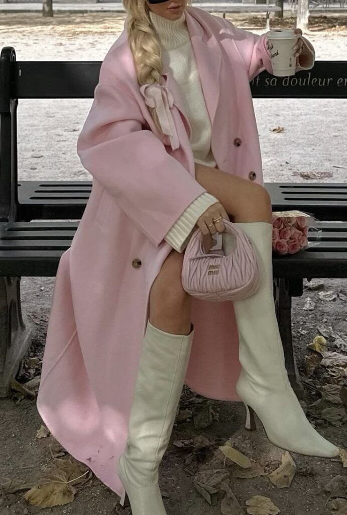 _ 48 Woman in a pink coat and white boots sitting on a bench, holding coffee and a handbag, with roses beside her. Fashionable and stylish. | Sky Rye Design Woman in a pink coat and white boots sitting on a bench, holding coffee and a handbag, with roses beside her. Fashionable and stylish.