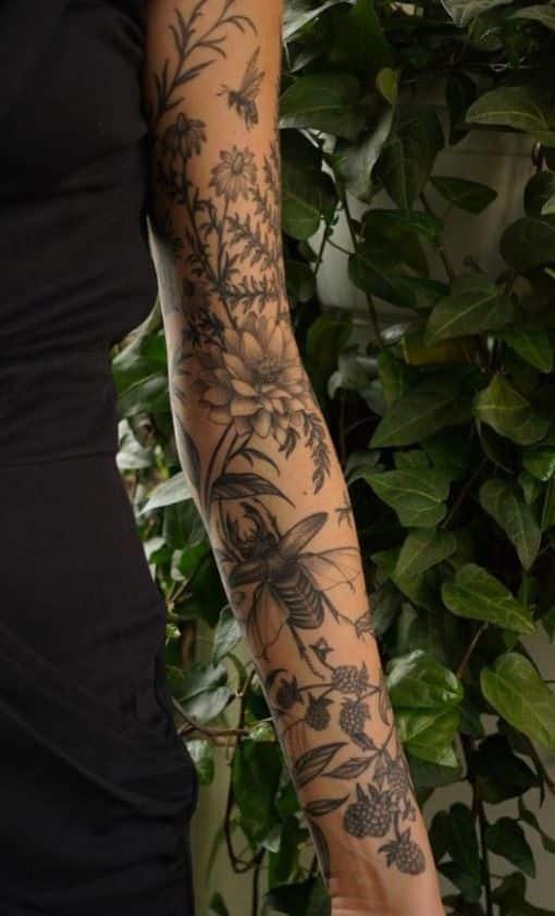 4cb04a39-703f-4a97-8324-2bbf0667ed87 Arm with detailed floral and bee tattoos against a backdrop of lush green leaves, showcasing intricate ink art. | Sky Rye Design Arm with detailed floral and bee tattoos against a backdrop of lush green leaves, showcasing intricate ink art.