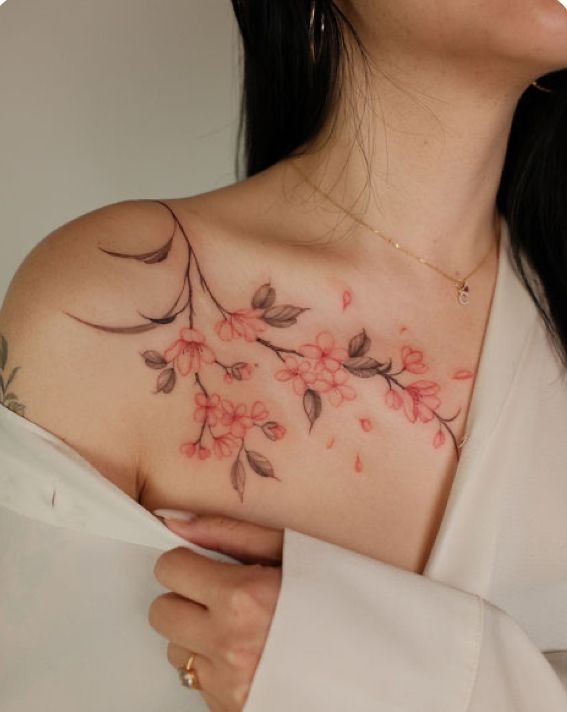 5b751fdf-0930-4650-9722-e3c9d78c8427 Elegant cherry blossom tattoo on a woman's shoulder, featuring delicate pink flowers and soft green leaves, styled in a minimalist design. | Sky Rye Design Elegant cherry blossom tattoo on a woman's shoulder, featuring delicate pink flowers and soft green leaves, styled in a minimalist design.