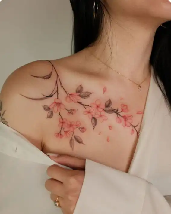 5b751fdf-0930-4650-9722-e3c9d78c8427 Elegant cherry blossom tattoo on a woman's shoulder, featuring delicate pink flowers and soft green leaves, styled in a minimalist design. | Sky Rye Design Elegant cherry blossom tattoo on a woman's shoulder, featuring delicate pink flowers and soft green leaves, styled in a minimalist design.