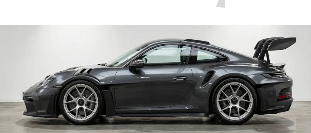 Sleek black sports car with large rear wing in showroom, side view showcasing aerodynamic design and alloy wheels.