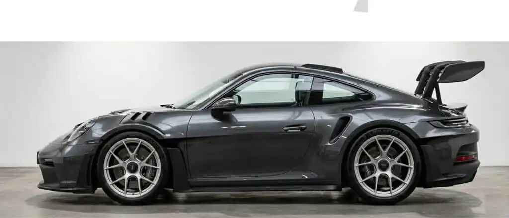 Sleek black sports car with large rear wing in showroom, side view showcasing aerodynamic design and alloy wheels.