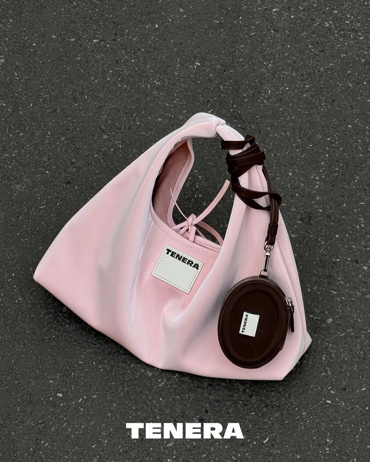 Pink Tenera handbag with round pouch and brown strap on textured surface. Fashionable accessory for stylish looks.