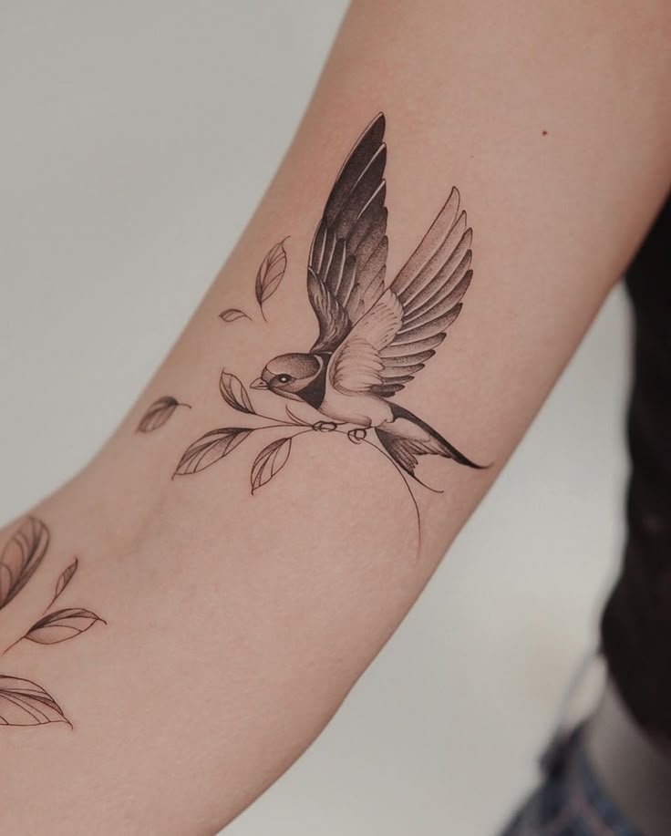 Elegant black and gray bird tattoo on forearm, showcasing intricate wings and branch details.
