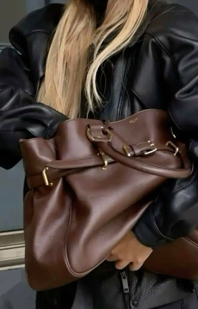 Woman in black leather jacket carrying a stylish brown leather handbag, showcasing elegant fashion accessories.