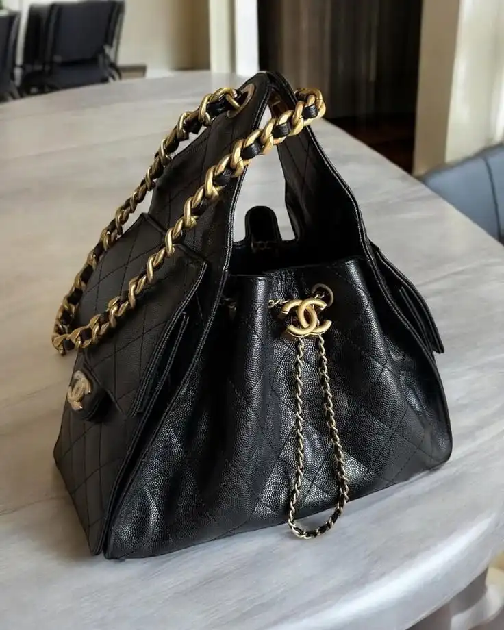 Luxury black leather handbag with gold chain detail on a table, featuring an elegant quilted pattern and distinctive logo accent.