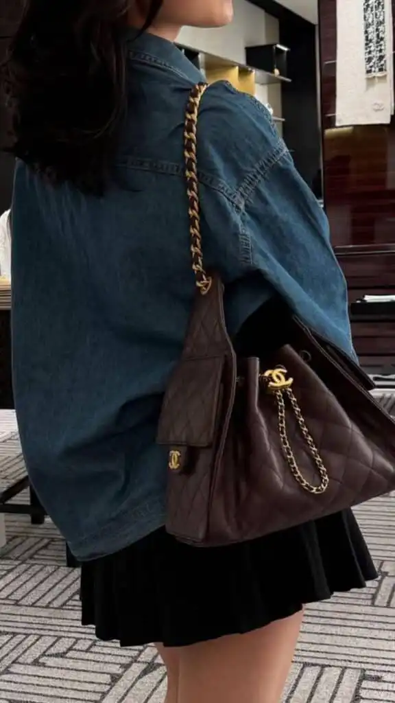 Stylish woman in denim jacket carrying a quilted designer handbag with gold chain in upscale setting. Fashion and elegance combine.