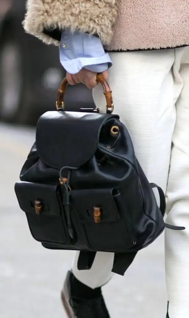 Stylish black leather backpack with bamboo handle, paired with a cozy jacket and white pants, perfect for a chic urban look.